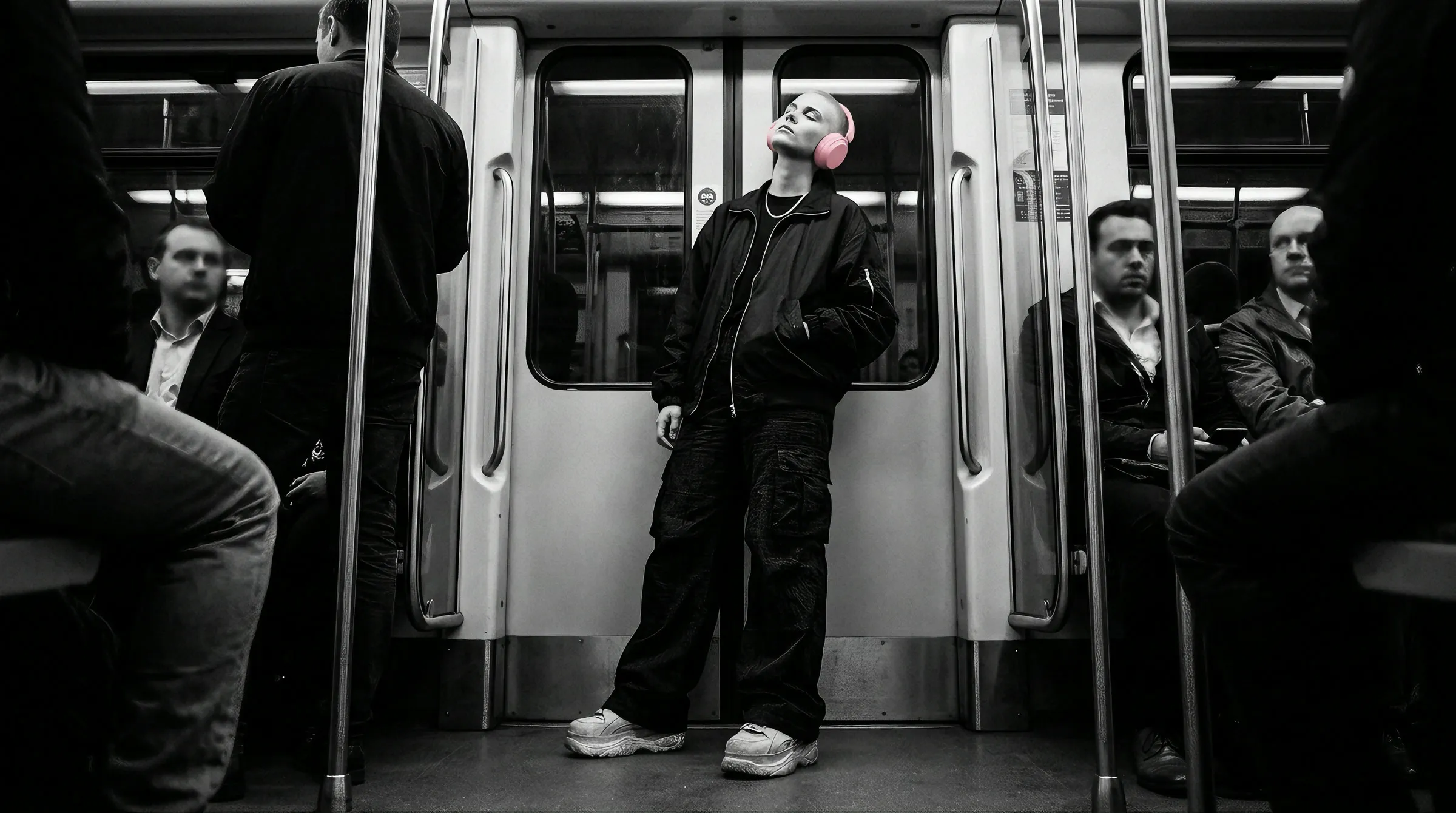 Low-angle shot of a model in blush pink headphones leaning against the doors of a crowded tram